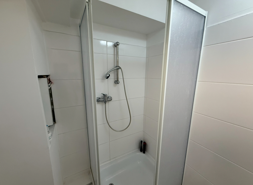 Duschkabine mit Glaswänden, weiß gefliest, silberne Duscharmatur, schlichtes, modernes Design.