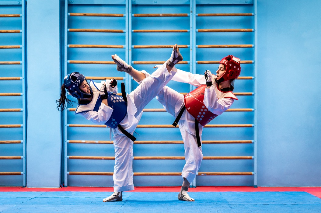 Portrait of two young women in kimono and suture, taekwondo athletes wrestling in the gym. Sportswomen demonstrating taekwondo martial art, hard training concept