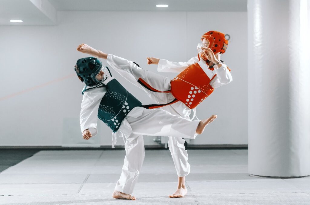 Sporty Caucasian boys having taekwondo training in white gym and kicking each other.