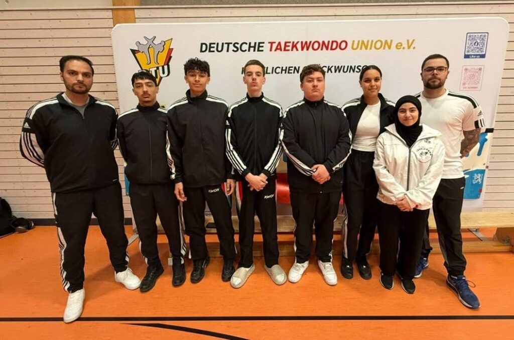 Eine Gruppe junger Menschen in Sportanzügen posiert ernst vor einem Banner.