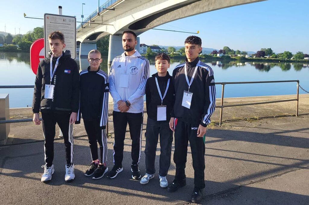Fünf Personen in Sportbekleidung stehen am Fluss, lächeln leicht und tragen Ausweise um den Hals.